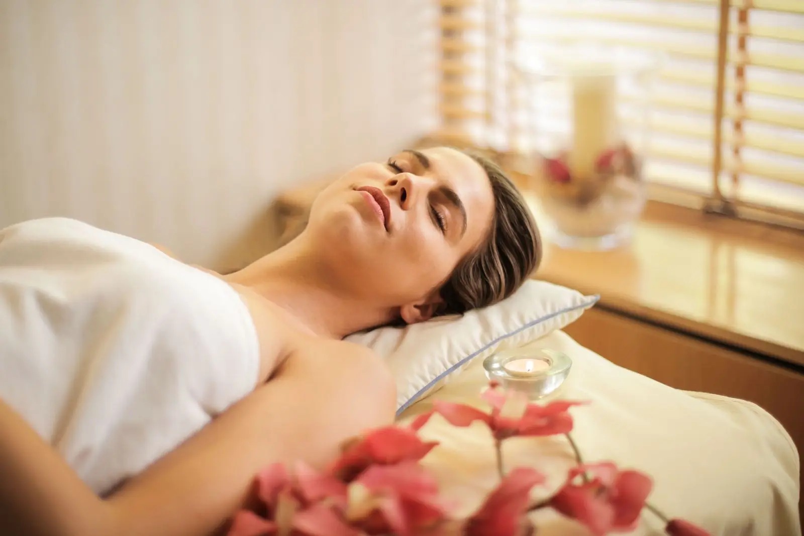 Femme détendue allongée sur une table de soin, bougie et fleurs à côté