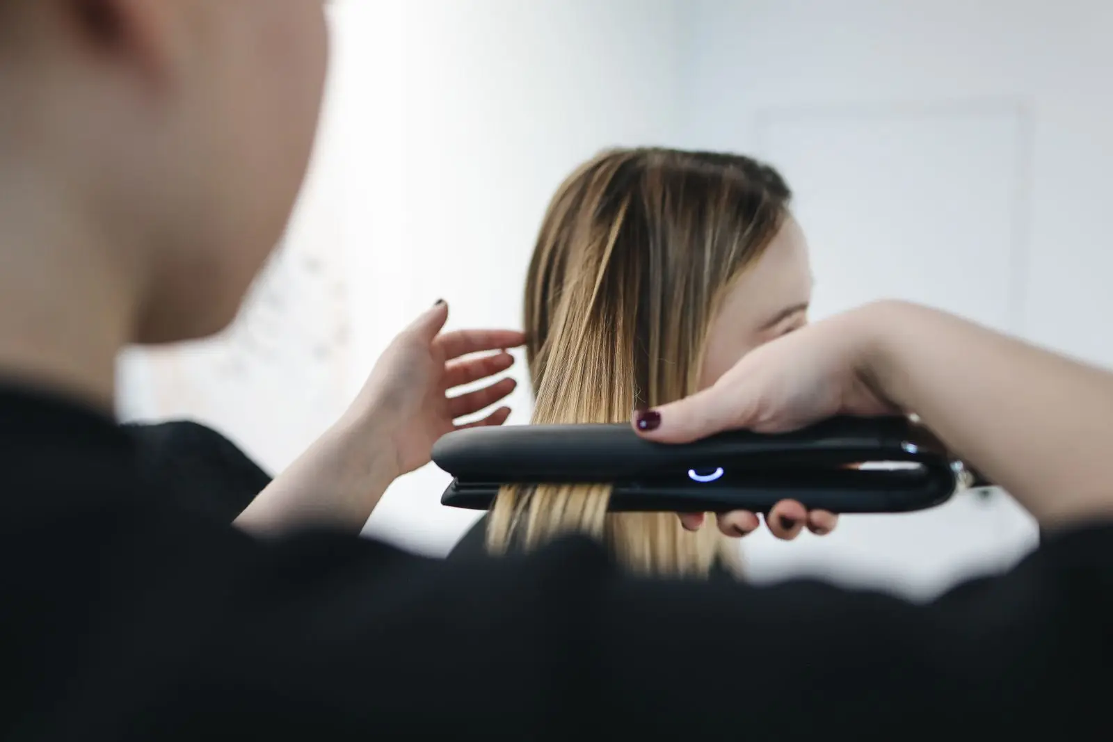 Coiffeuse lissant une longue mèche de cheveux avec un fer à lisser